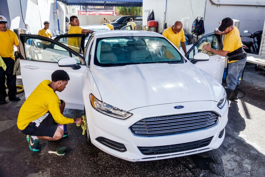 A white Ford Fusion at a car wash with several workers carefully polishing it