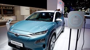 A blue Hyundai Kona Electric car sits on display next to a recharging unit.