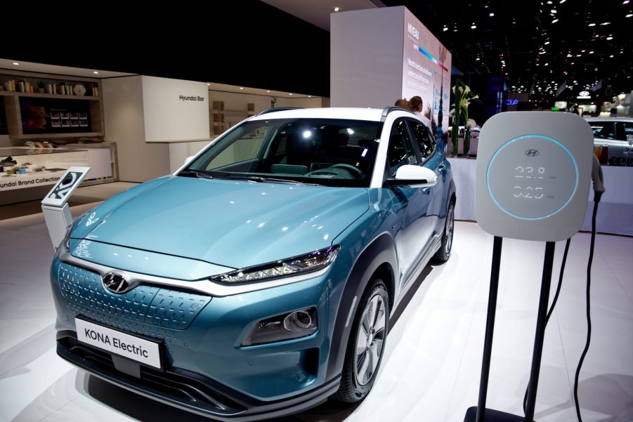 A blue Hyundai Kona Electric car sits on display next to a recharging unit.