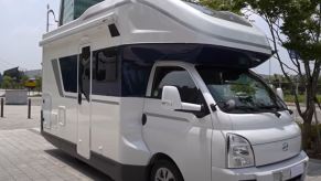 A white RV on a cab-over chassis is parked downtown.