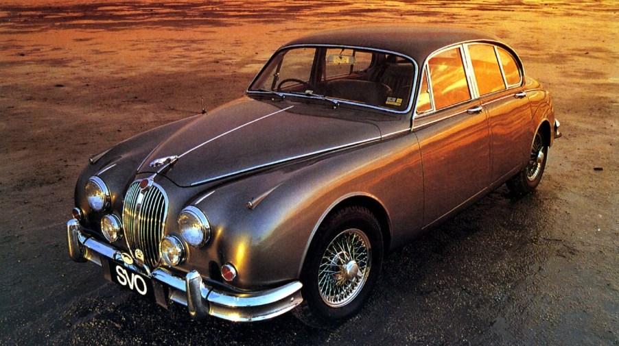 A silver-gray 1959 Jaguar Mk2 sedan on a damp sunset-lit track