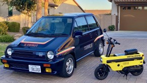 A blue 1983 Honda City Turbo II with a yellow unfolded Honda Motocompo scooter on a brick driveway