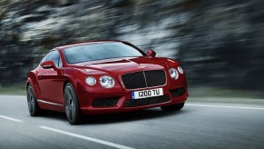 A red 2013 Bentley Continental GT V8 drives quickly down a forest road