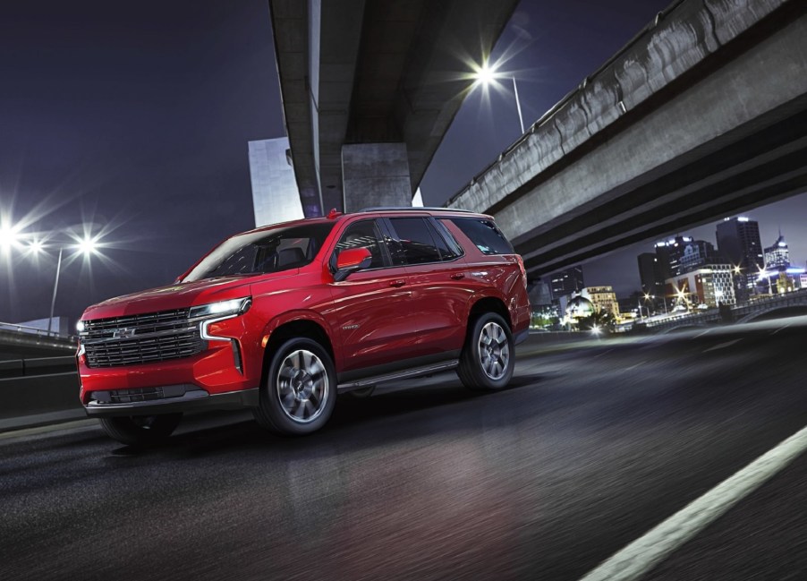 A red 2021 Chevrolet Tahoe drives on a city's highway at night