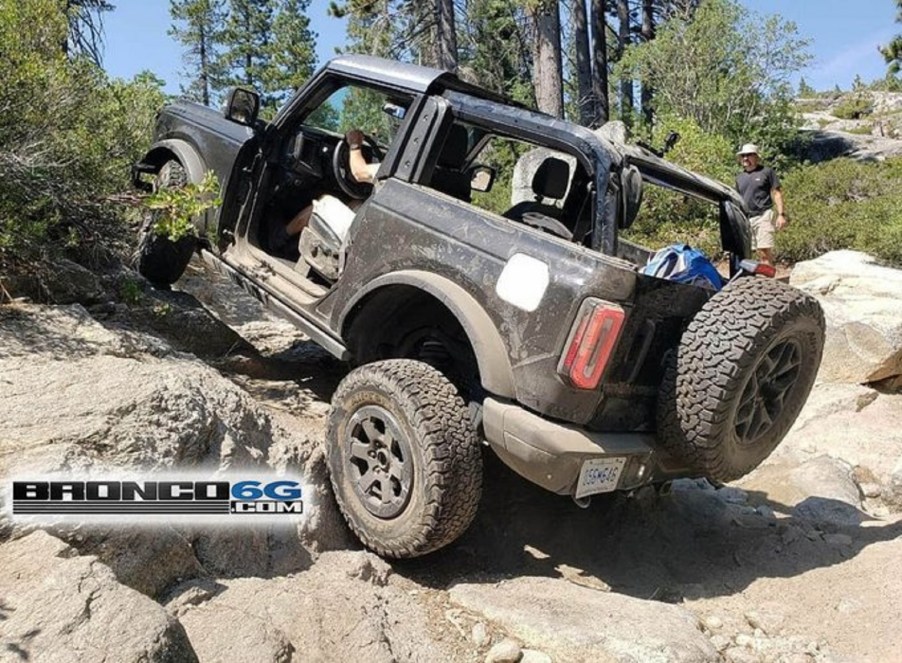 A black 2-door 2021 Ford Bronco with its doors and roof removed scrambles up a rocky incline on the Rubicon Trail