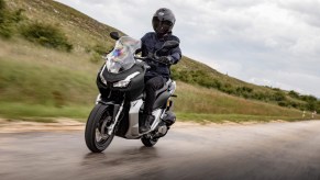 A black 2021 Honda ADV150 rides down a wet road