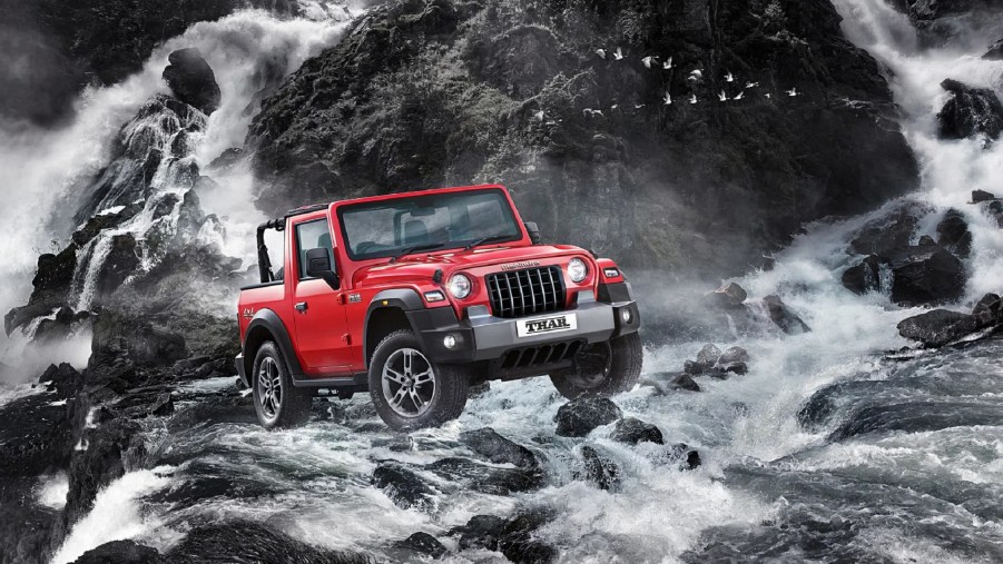 A red 2021 Mahindra Thar with its roof off crosses a roaring river