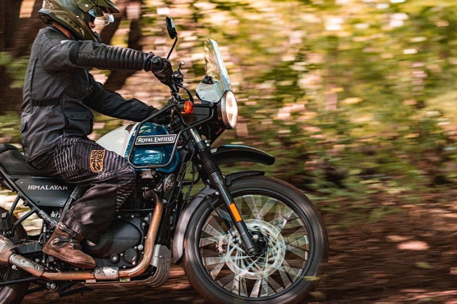 A rider guides a blue-and-white 2021 Royal Enfield Himalayan through a forest