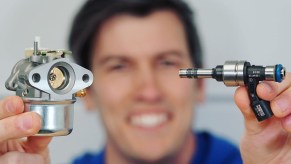 Jason Fenske of Engineering Explained holds a carburetor in his right hand and an electronic fuel injector in his left hand