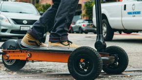 A black and orange electric scooter is shown with somebody riding it in an urban setting.