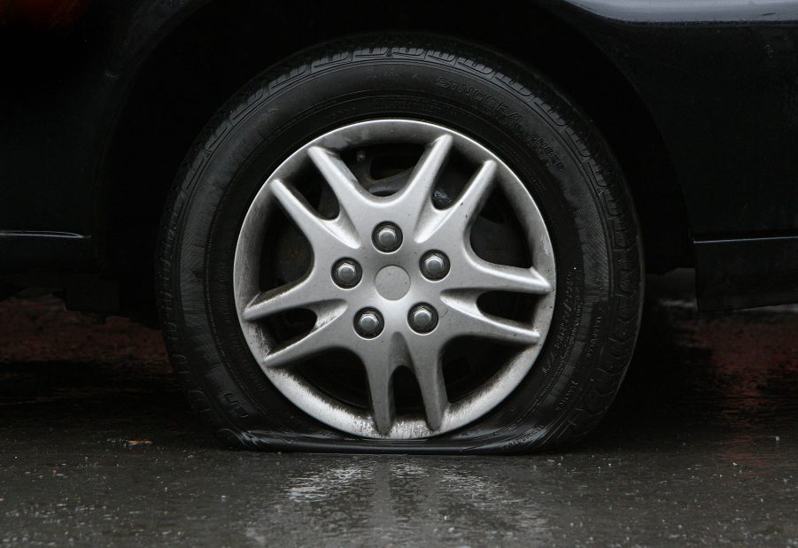 A flat tire on a car is seen on a wet pavement surface.