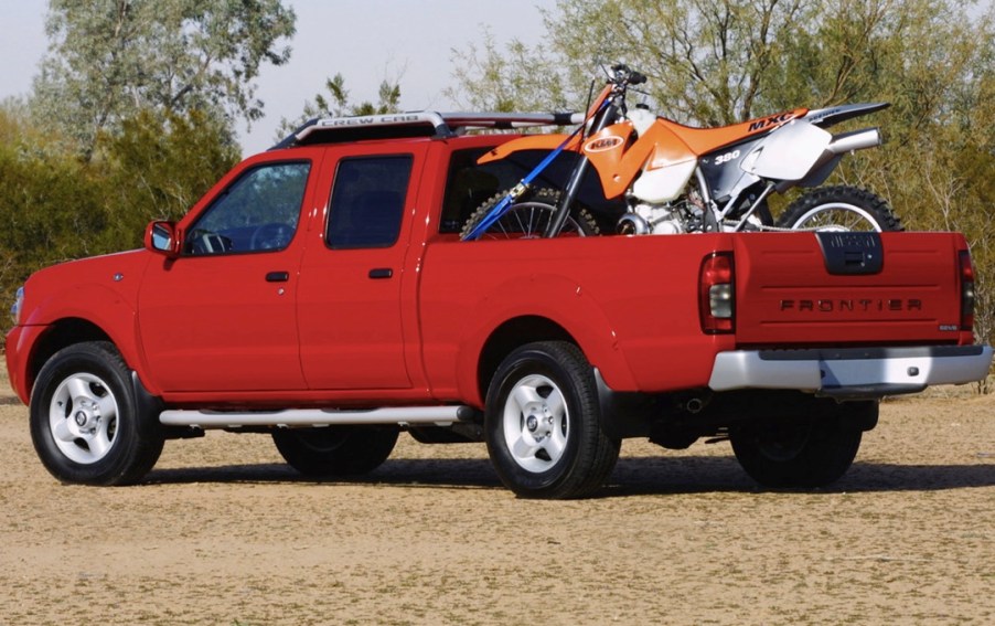 a red crew cab Nissan Frontier from the 2004 model year with a dirt bike in the back is a perfect example of one of the best used pickup trucks to buy