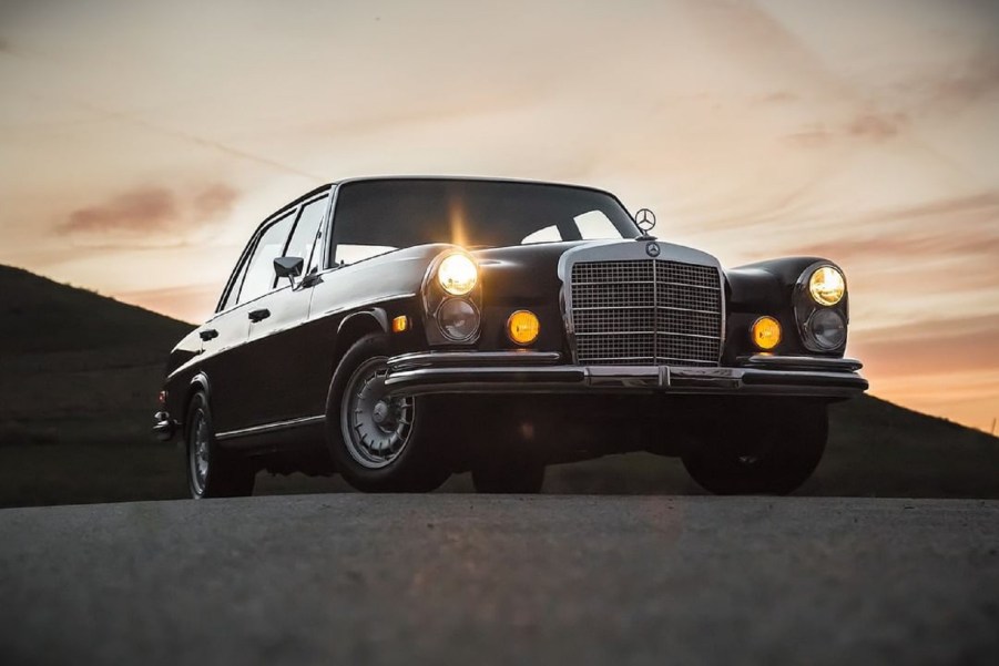 A black Mercedes 300SEL 6.3 in the desert at sunset with its lights on