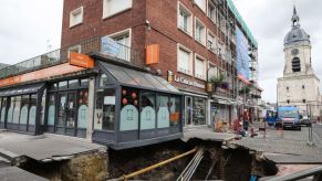 Construction workers stand near a sinkhole along a street in the city of Amiens, northern France, on August 13, 2019. - A five metres deep and ten metres wide sinkhole appeared in the centre of Amiens overnight on August 11, which the local municipal services believe could have been triggered by the collapse of a medieval cave in the vicinity. (Photo by DENIS CHARLET / AFP) (Photo credit should read DENIS CHARLET/AFP via Getty Images)