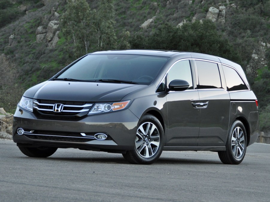 A grey 2015 Honda Odyssey parked near a green mountain.