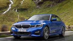 a blue 3 Series at speed on a scenic mountain road.