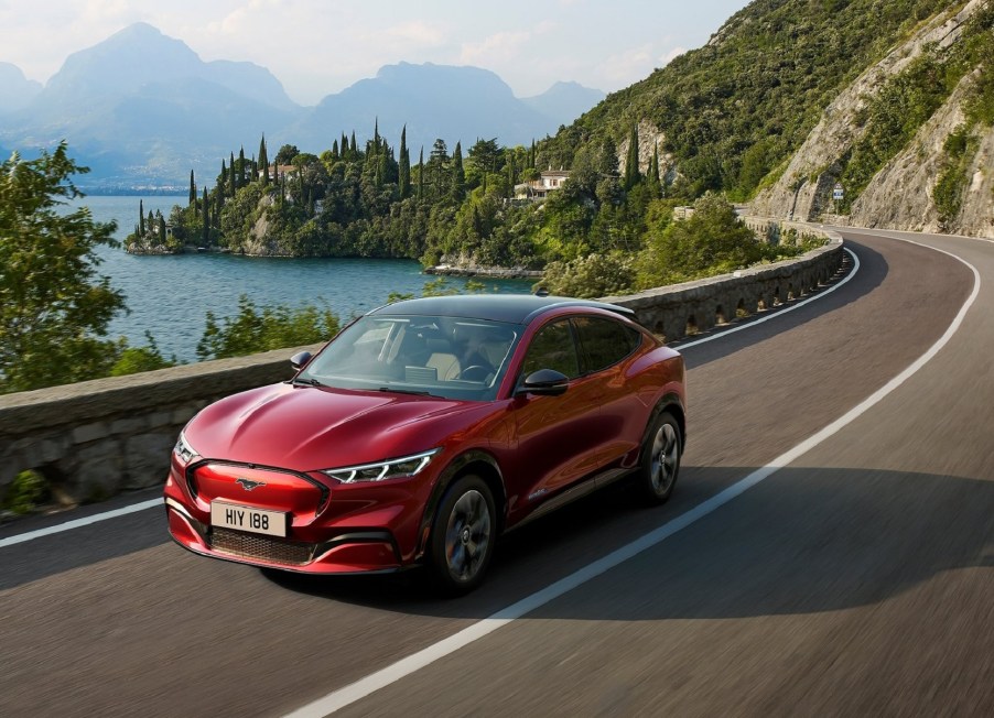 A red 2021 Ford Mustang Mach-E drives next to a lake