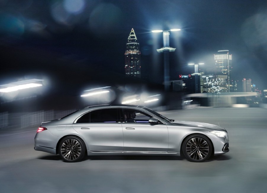 A silver 2021 Mercedes S-Class drives through a bright-lit night city