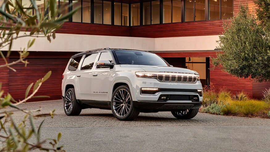 A white Jeep Grand Wagoneer is seen parked on a driveway before a garage