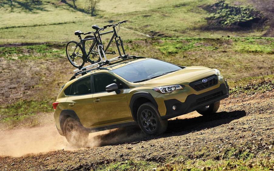 a gold 2021 subaru Crosstrek subcompact crossover SUV off-roading with a loaded bike rack up top.