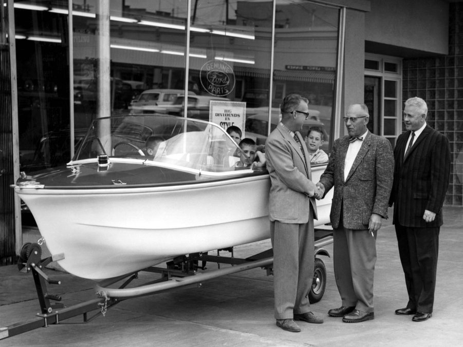 Men shaking hands at boat dealership, 1960s