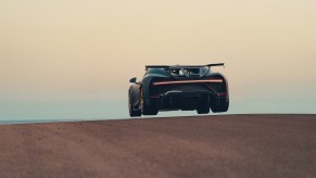 The silhouette of the rear of a car getting airborne cresting a small hill.