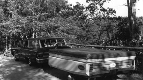 An old black and white photo of a family towing a pop-up camper