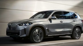 A gray BMW X5 midsize SUV is driving on the road.