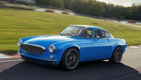 A blue Volvo P1800 Cyan restomod drives around a racetrack