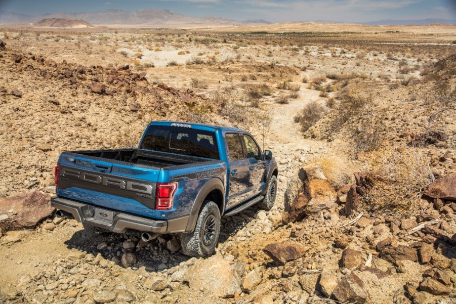 Blue Ford F-150 Raptor driving on gravel desert road