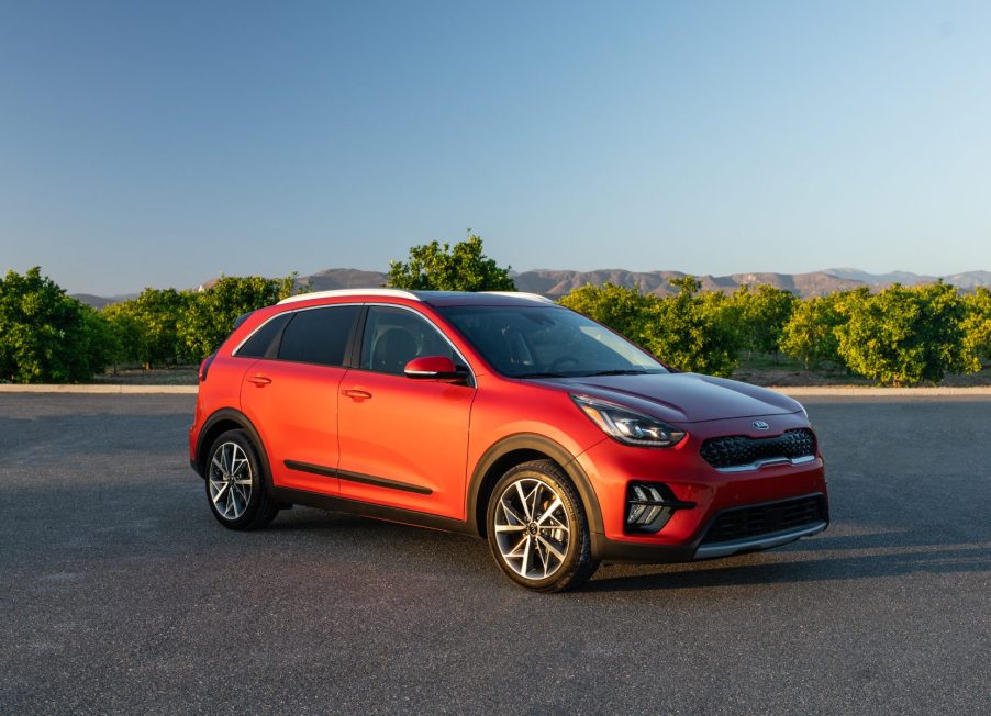 An orange 2020 Kia Niro on display in a parking lot with trees in the background