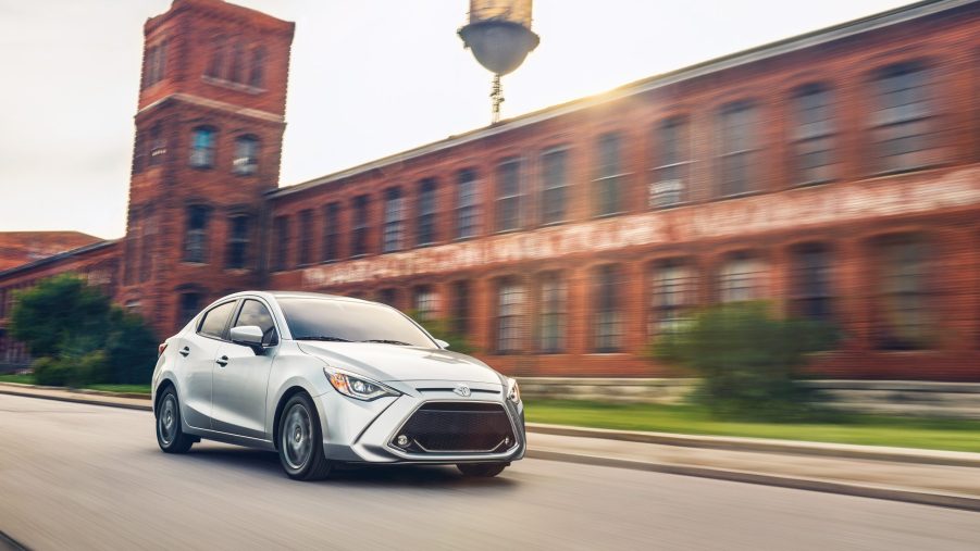 A grey Toyota Yaris drives down a road past a factory