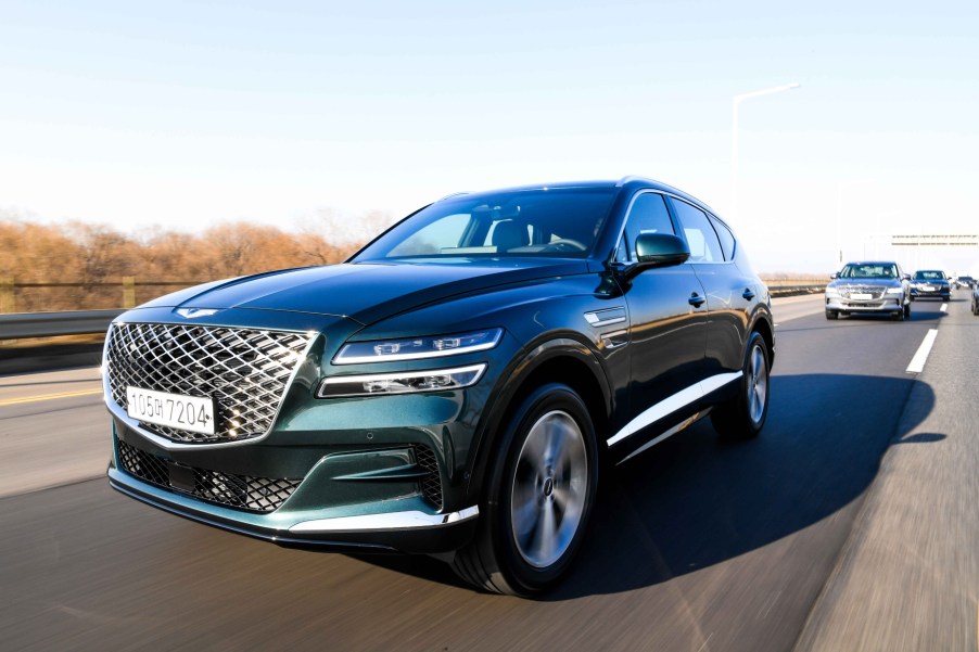 A front-facing shot showing off Genesis' signature grille on a green 2021 GV80 driving down the highway