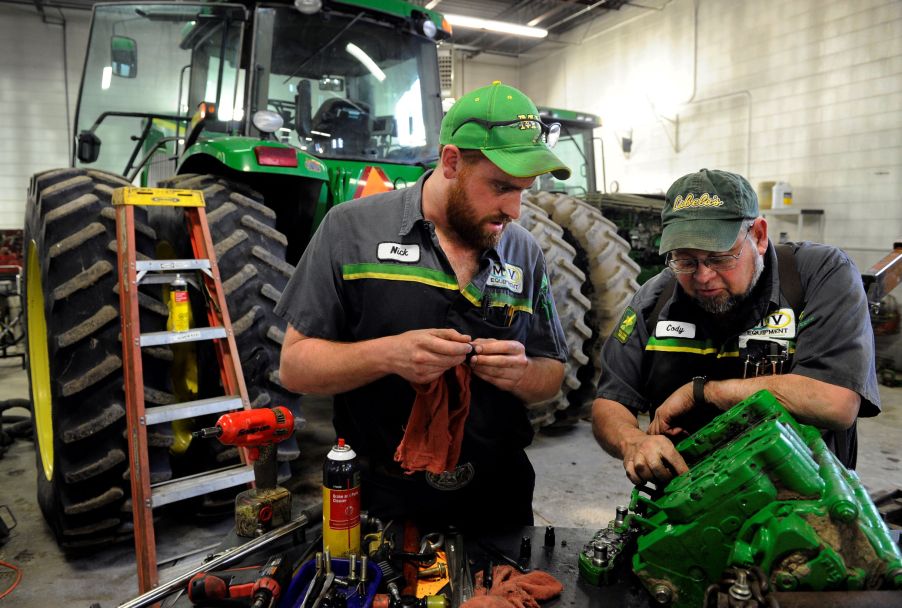 A master mechanic and service technician repair a John Deere tractor in a garage