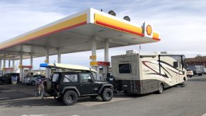 An RV tows a Jeep and outdoors gear while filling up its gas tank