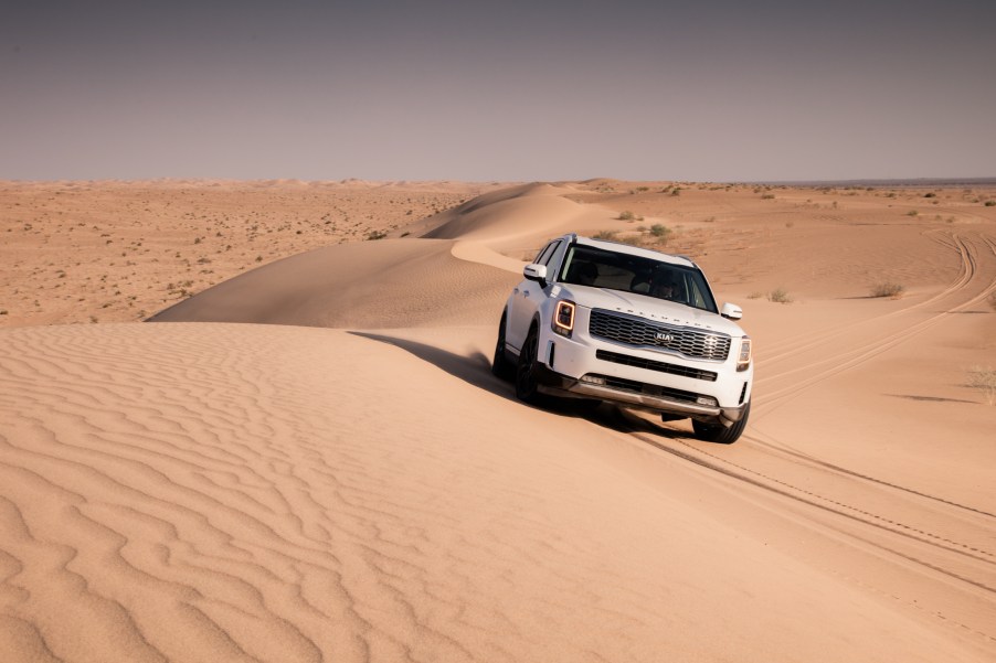 A white Kia Telluride is traveling on sand dunes.