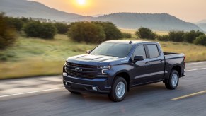 A 2020 Chevy Silverado 1500 driving on the road with trees and the sun in the background