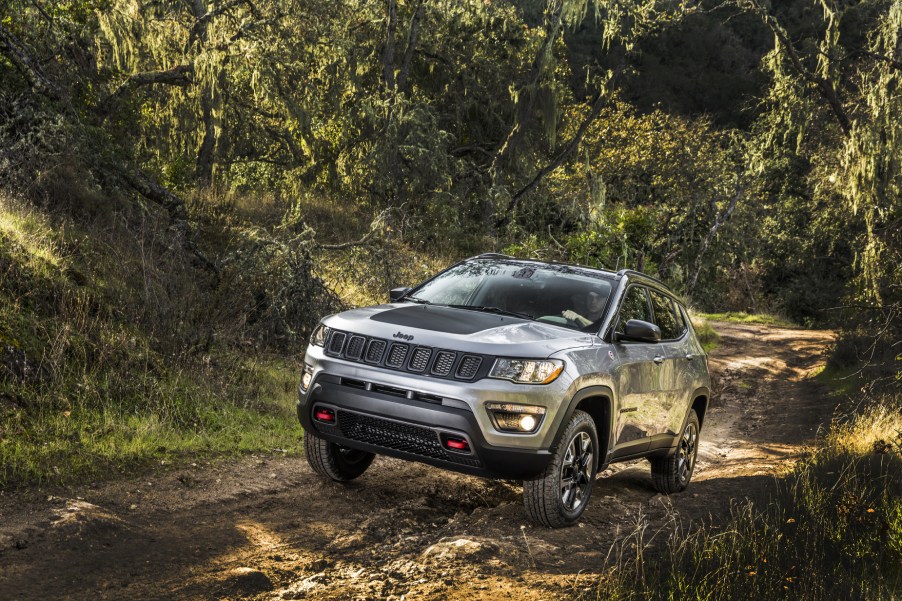 A silver 2020 Jeep Compass driving down a trail in the woods