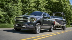 A grey 2021 Ford F-150 PowerBoost towing a boat on highway