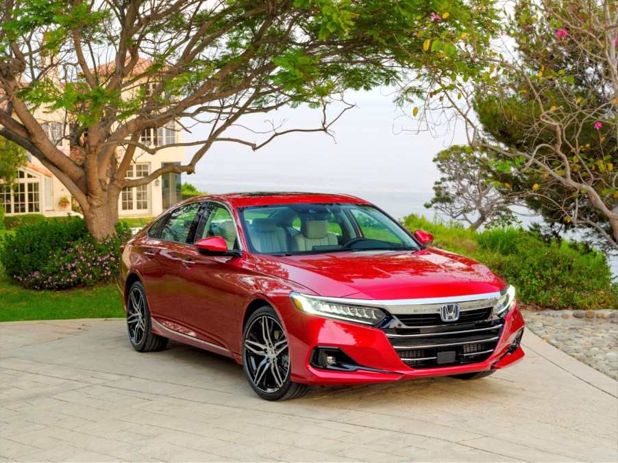 A red 2021 Honda Accord Hybrid parked in front of a house with trees in the background