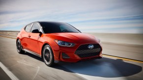 An orange 2021 Hyundai Veloster driving down a road