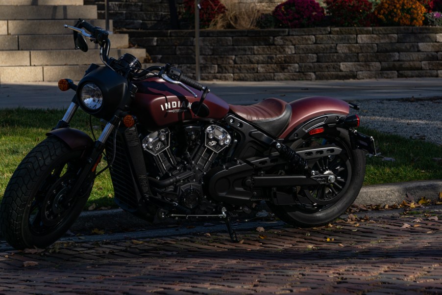 A maroon 2021 Indian Scout Bobber parked on a shady cobblestone road