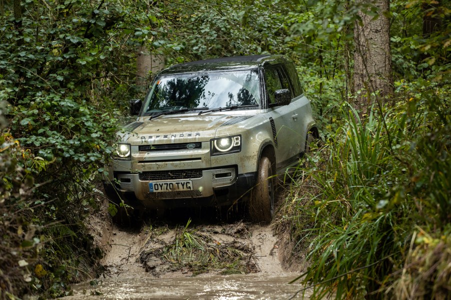 A 2021 Silver Land Rover Defender drives on rough terrain.