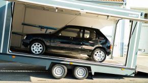 A black pre-restoration Peugeot 205 GTI in a trailer