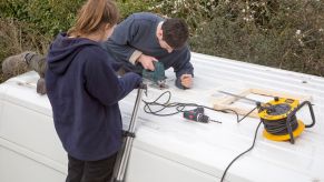 Cutting through roof of white metal camper van conversion to install ventilation window