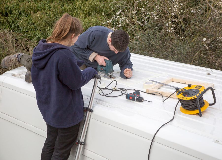 Cutting through roof of white metal camper van conversion to install ventilation window