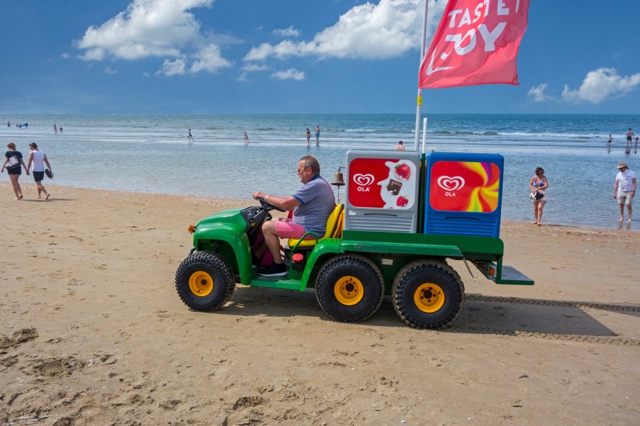 John Deere Gator transformed into ice-cream truck sells ice cream to tourists on the beach at a seaside resort on the North Sea coast.