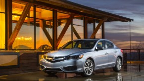 A silver 2016 Acura ILX parked in front of a wood building with large windows and a sunset in the background