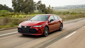 A red 2019 Toyota Avalon drives on a foliage-lined road outside a city.