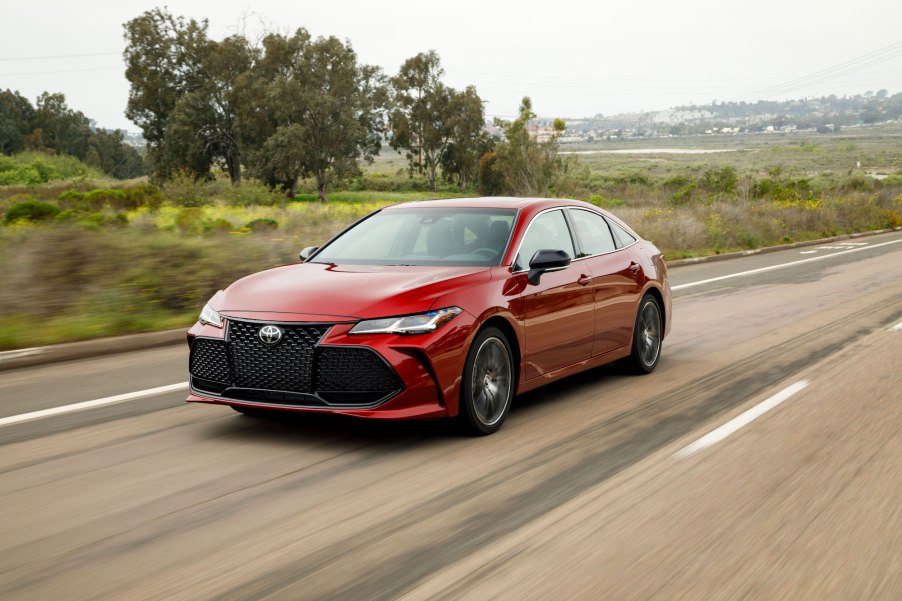 A red 2019 Toyota Avalon drives on a foliage-lined road outside a city.